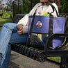 A Large upcycled tote bag sitting on a bench with a women behind it wearing a repaired knit sweater