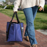 A Women wearing a repaired sweater walking with a large upcycled tote bag