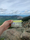 A Small yellow Trail Wallet being held with a view of Cannon Cliffs in New Hampshire in the background.